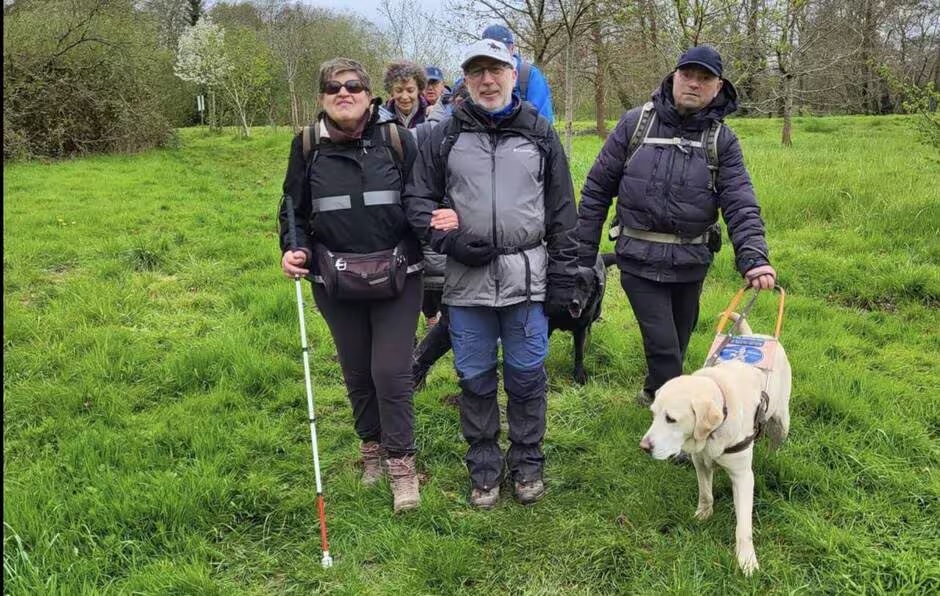 Photo illustrant l'article de Ouest-France du 10 avril 2024 sur l'obtention d'un trophée par la section Randonnée du HRC. File de randonneurs du HRC (déficients visuels et accompagnants) traversant un champ dans la campagne